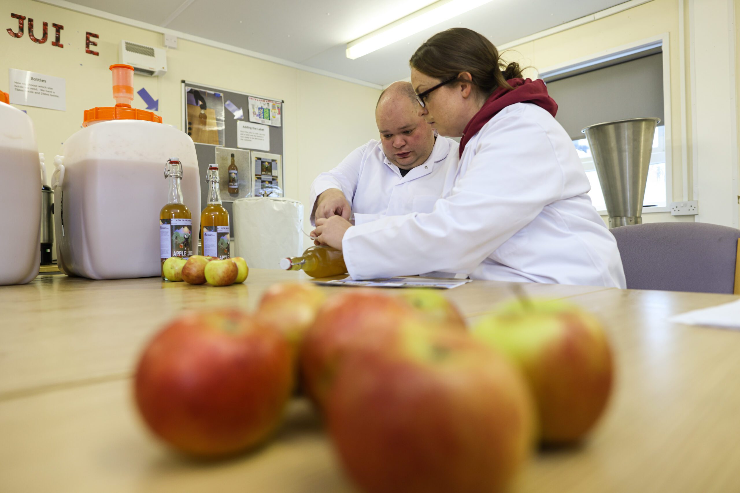 Two people working in an apple pressing plant, with apples in the foreground