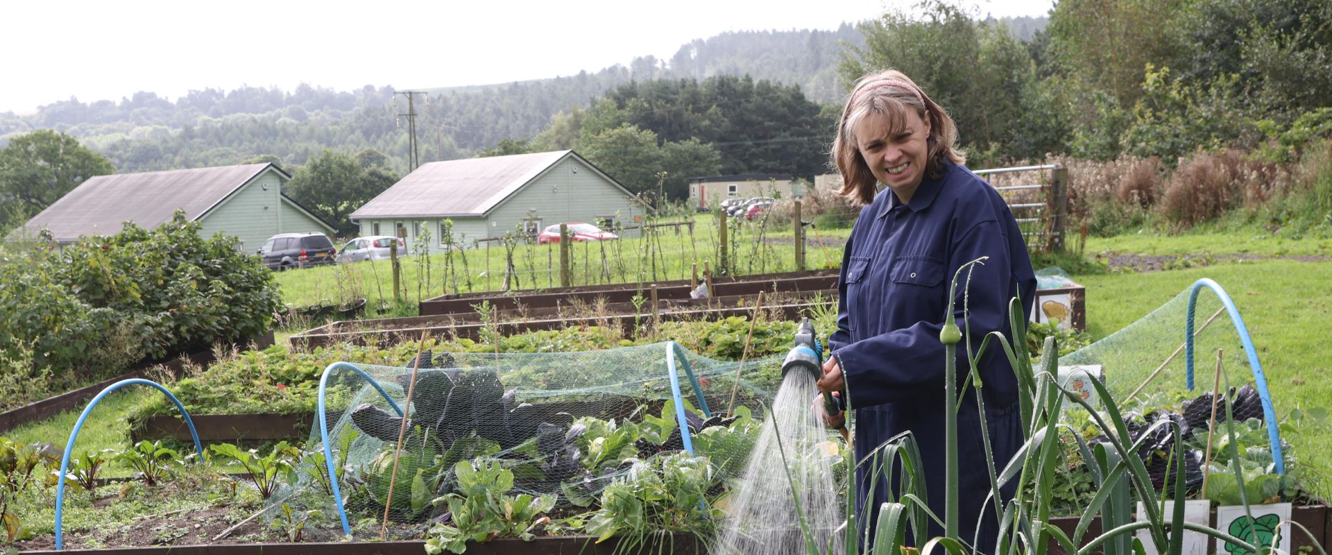 A woman in overalls waters vegetables