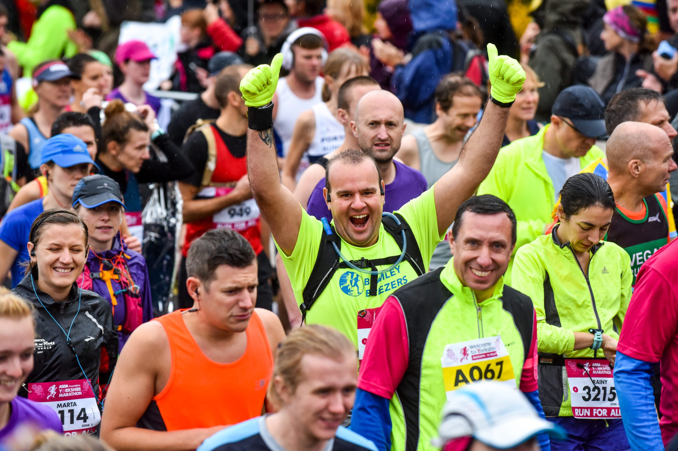 A runner among an event crowd giving two thumbs-up to the camera